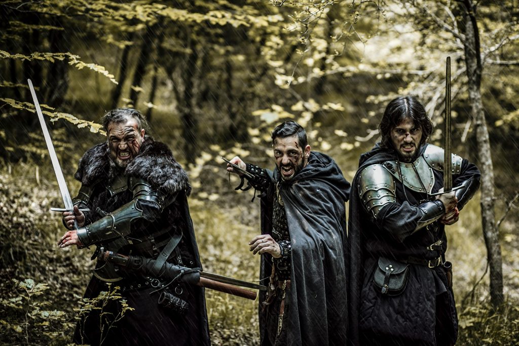 Three men in medieval armor and swords standing in a forest, ready for battle.